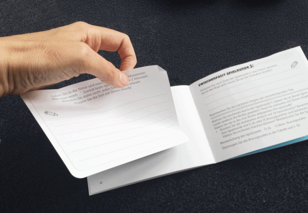 Hand blättert im Kairos Spieljournal von Rotmont – Coaching-Notizbuch aufgeklappt auf dunklem Untergrund