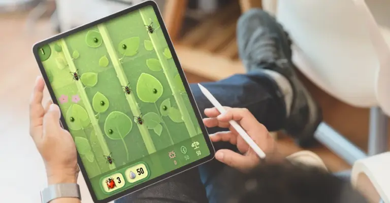 Hände halten ein Tablet mit grünem Spielfeld und spielerischen Elementen.